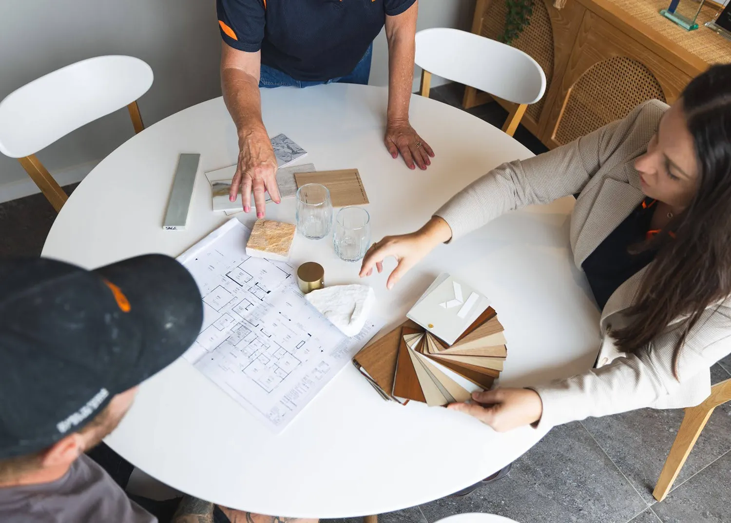 three people sitting at a round table looking at construction plan and natural colour samples.